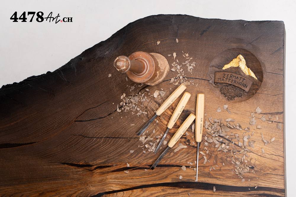 Schnitzeisen, Klüpfel und Späne auf einer Platte aus Mooreiche, daneben das geschnitzte Matterhorn mit Gold