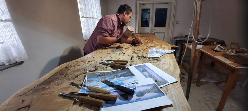 Der Schnitzer bei der Arbeit an der Platte, davor Fotos des Stellisees als Vorlage